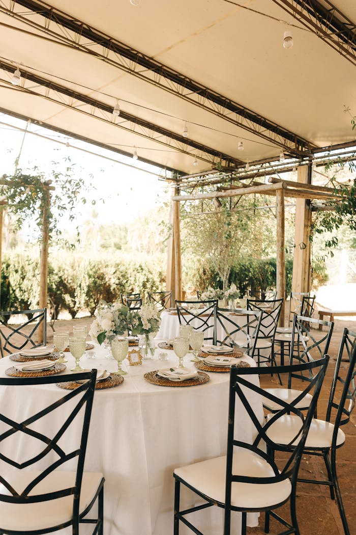 Elegant outdoor wedding reception with beautifully decorated tables and chairs under a canopy.