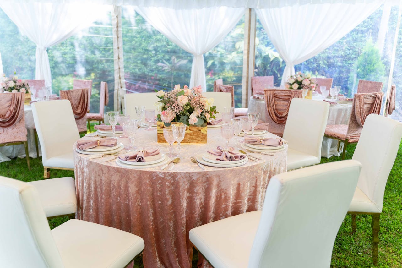 Chic outdoor wedding reception setup with floral centerpieces and draped chairs under a white marquee.